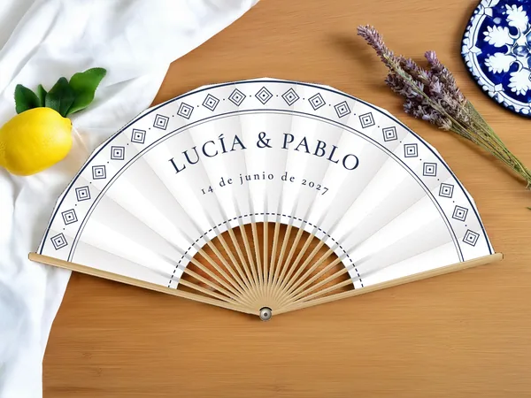 Abanico de boda personalizado «Azulejo», tela blanco e impresión en azul marino, sobre una mesa de boda