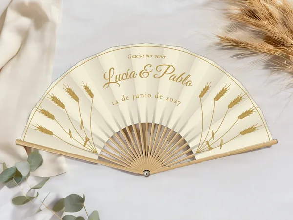 Abanico de boda personalizado «Espigas de trigo», tela marfil e impresión en oro, sobre una mesa de boda