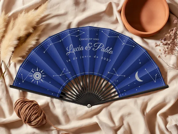 Abanico de boda personalizado «Celeste», tela azul marino e impresión en plata, sobre una mesa de boda