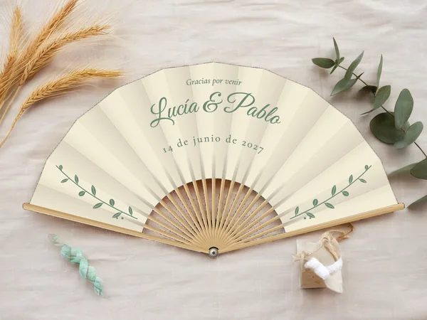 Abanico de boda personalizado «Eucalipto», tela marfil e impresión en verde salvia, sobre una mesa de boda