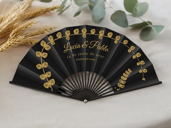 Abanico de boda personalizado «Eucalipto dorado», tela negro e impresión en oro, sobre una mesa de boda
