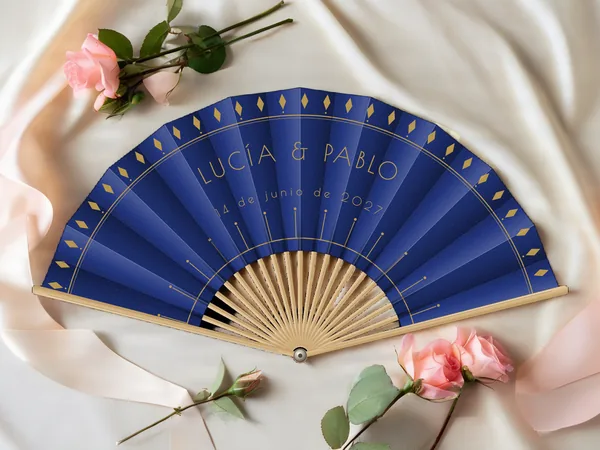 Abanico de boda personalizado «Gatsby», tela azul marino e impresión en oro, sobre una mesa de boda