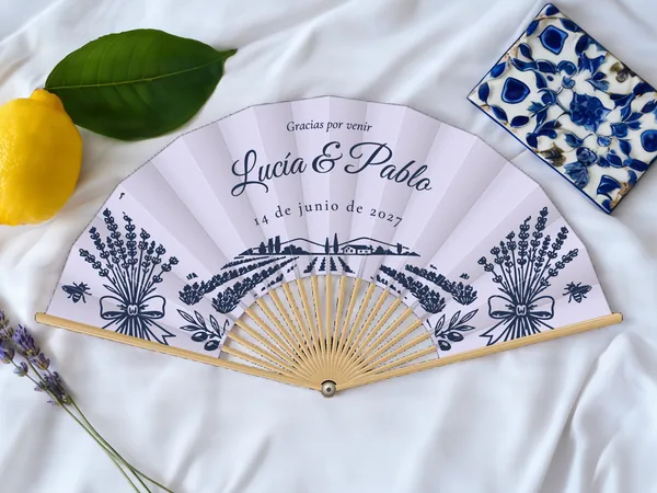 Abanico de boda personalizado «Campo de lavanda», tela lavanda e impresión en azul marino, sobre una mesa de boda