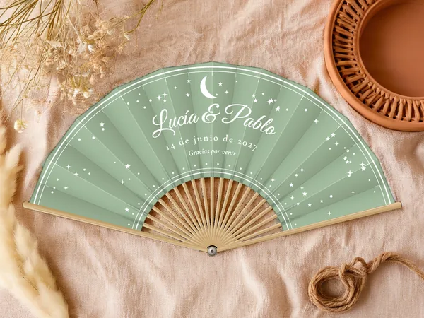 Abanico de boda personalizado «Luna y estrellas», tela verde salvia e impresión en blanco, sobre una mesa de boda