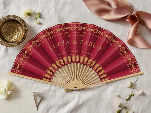 Abanico de boda personalizado «Medina», tela burdeos e impresión en oro, sobre una mesa de boda