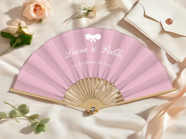 Abanico de boda personalizado «Lazo», tela rosa empolvado e impresión en blanco, sobre una mesa de boda