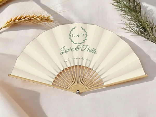 Abanico de boda personalizado «Corona de olivo», tela marfil e impresión en verde salvia, sobre una mesa de boda