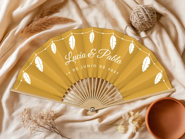 Abanico de boda personalizado «Plumas», tela mostaza e impresión en blanco, sobre una mesa de boda