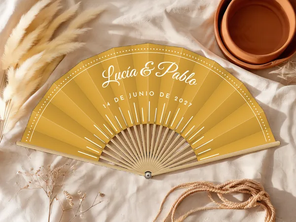Abanico de boda personalizado «Rayos de sol», tela mostaza e impresión en blanco, sobre una mesa de boda