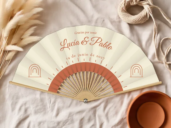 Abanico de boda personalizado «Sol boho», tela marfil e impresión en terracota, sobre una mesa de boda